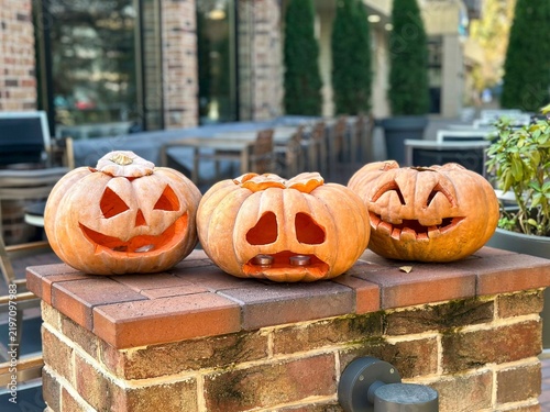 Quadro su tela Three carved Halloween pumpkins with glowing candlelit faces on a brick pillar