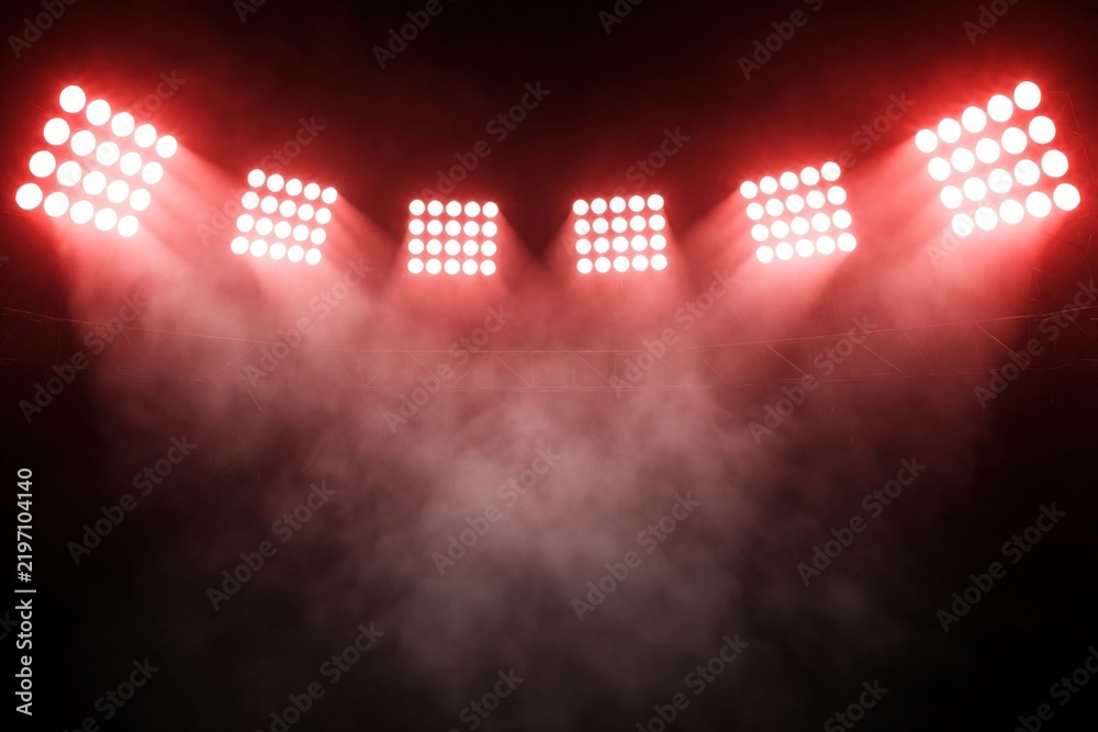 Obraz premium Red stadium lights illuminate a dark arena filled with smoke. Bright spotlights create a dramatic atmosphere. This empty venue glows with intense energy, perfect for sporting events or concerts.