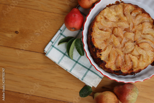 Traditional french cake Tart Tatin with sliced pears on a plate on wooden table with pear fruits and copy space