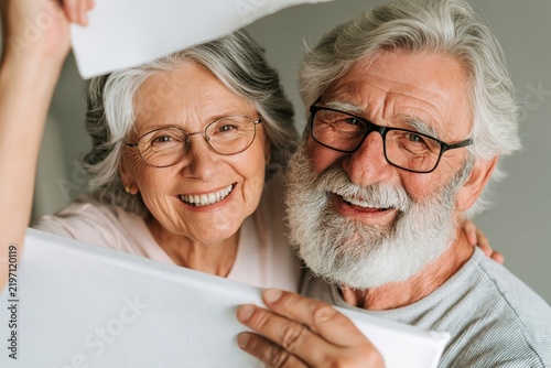 Happy senior couple smiling together while holding white canvas frames at home
