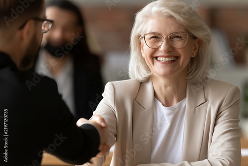 Smiling senior businesswoman shaking hands with business partner during successful meeting