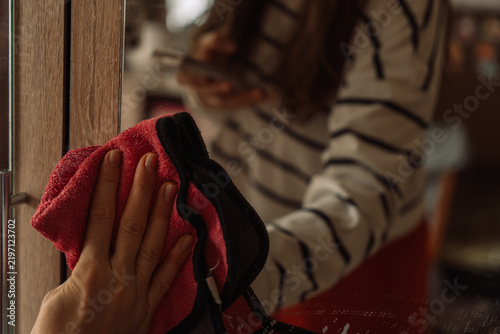 Hand wiping a mirror with a red cloth beside a woman's reflection.