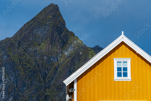 Traditional yellow wooden cabin against a dramatic mountain.