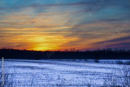 Fotografie A bright sun disk disappears behind the horizon, painting the sky with rich gold, orange, and blue hues