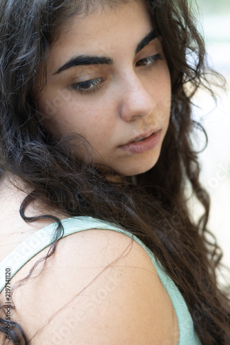 Young woman with dark wavy hair looking thoughtful outdoors