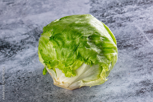 Fotografía Fresh green iceberg lettuce head on textured gray surface, crisp leaves and whit