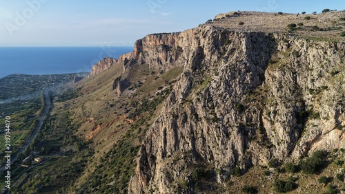 Aerial view of the rugged coastal cliffs of Terrasini, featuring steep rocky slopes, sparse vegetation, and a view of the Mediterranean Sea along the coastline in Terrasini, Sicily, Italy.
