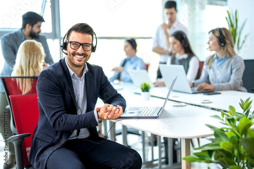 Call center representative wearing headset sitting at desk with laptop in open space office.