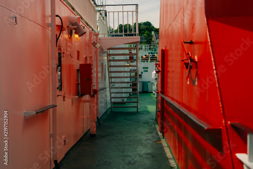 Konstfotografi Metal staircase and railings between pink and red superstructures on the deck of a ship or ferry - 4 September 2026