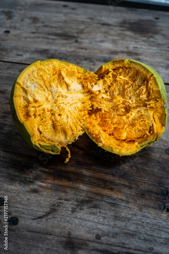 Close‑up of bael fruit (Aegle marmelos) and split ripe squash with bright orange fibrous flesh and green skin on rustic wooden table.