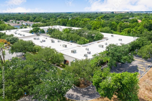 Top down view of a commercial building rooftop surrounded by lush green trees with flat roof office complex business park hvac systems building exterior corporate office