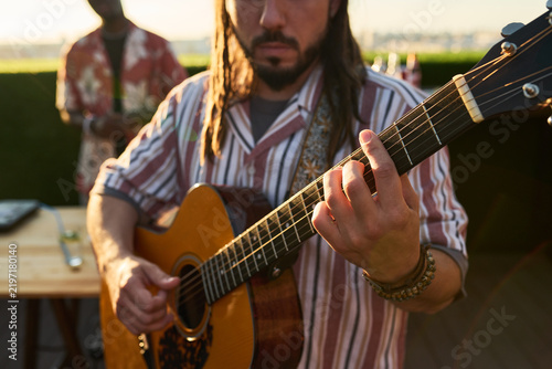 Принти на полотні Caucasian young adult man playing acoustic guitar with friend during outdoor music performance