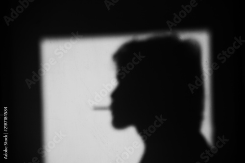 Close up side view black and white shadow of a man smoking cigarette on the dirty wall