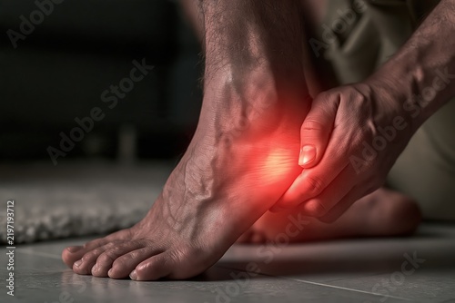 Man holding painful foot with sore heel and ankle injury medical care