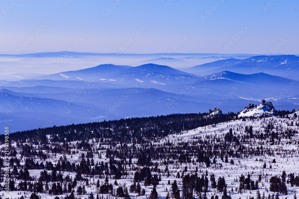 Fototapeta premium Panoramic view of mountain ridges covered morning mist and blue pink pastel colored sky. Distant peaks fade smoothly in horizon, creating depth effect under clear winter sky. Scenic landscape.
