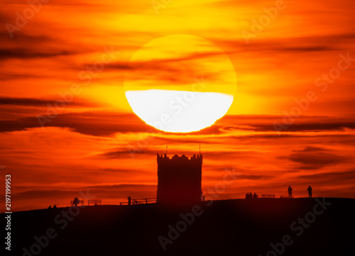 Stunning image of Rivington Pike Tower silhouette against a spectacular sunset with people watching the sun slowly set at Rivington, Chorley, Lancashire, England 
