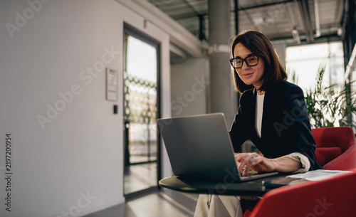 Smiling businesswoman typing on a laptop in a modern office lounge
