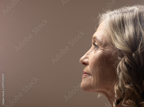 Senior woman posing in strict profile at studio showing face gray hair neutral backdrop, copy space