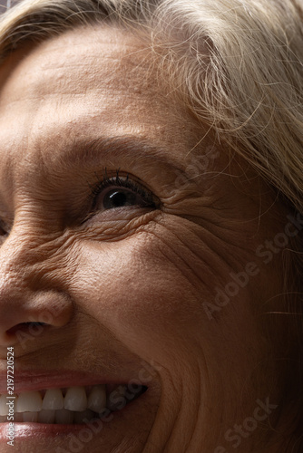 Senior woman smiling, showing crow's feet, lip lines, teeth, eyelashes and grey hair in studio