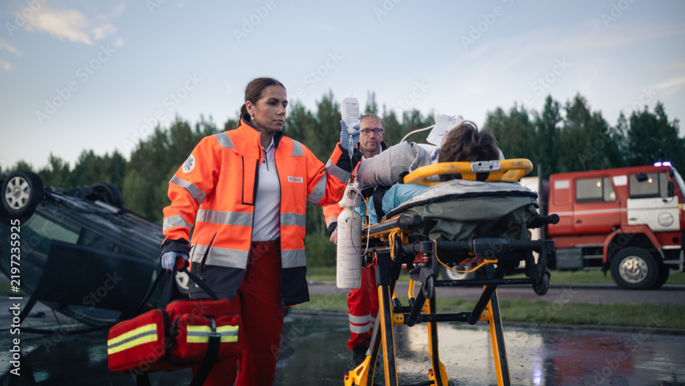 Obraz premium Paramedic Team Transporting Injured Victim on Stretcher With Iv Drip and Oxygen After Car Crash, Overturned Vehicle and Fire Truck at Traffic Accident Scene During Evening Rescue Operation
