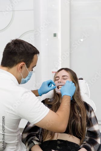 Obraz na płótnie Dentist placing cheek retractor on smiling female patient in dental chair, dental examination procedure with mouth opener, orthodontic checkup in clinic