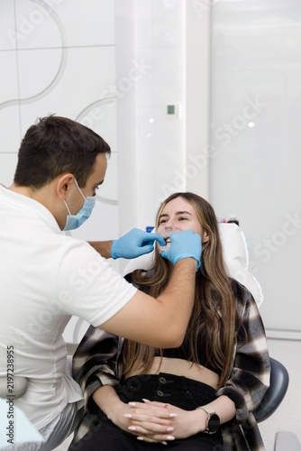 Konstfotografi Dentist placing cheek retractor on smiling female patient in dental chair, dental examination procedure with mouth opener, orthodontic checkup in clinic