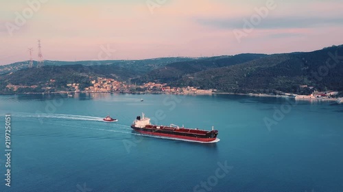 Aerial view of a large tanker vessel accompanied by a pilot boat navigating through calm waters in the soft light of early morning, representing global maritime trade and shipping logistics.