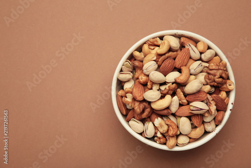 Mix of various nuts in bowl on brown background. Pistachios, cashews, walnuts, hazelnuts, peanuts.