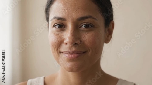 A close-up portrait of a smiling woman with dark hair and brown eyes, looking directly at the camera.