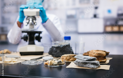 Fotografía Scientist in blue gloves examines mineral and rock samples beside a microscope in a modern laboratory