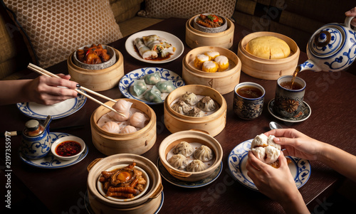 Delicious Cantonese dim sum feast spread bamboo steamers shrimp dumplings steamed buns pork ribs rolls chicken feet tea pouring restaurant banquet dining experience