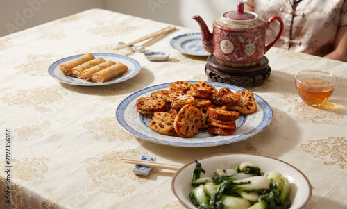 Traditional Chinese family dinner feast roasted lotus root stuffed slices spring rolls vegetable stir fry porcelain teapot tea cups banquet spread culinary heritage culture