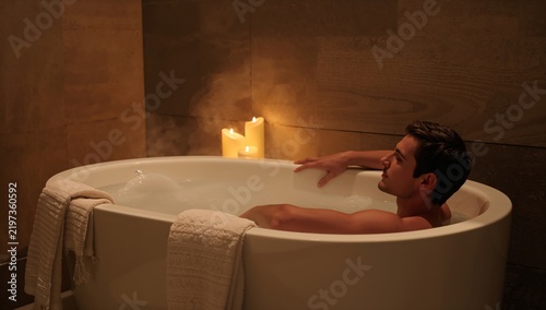 Man Relaxing in Bathtub With Candles at a Spa in the Evening