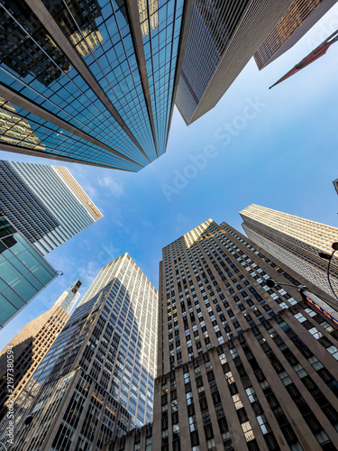 Low angle view of modern skyscrapers in Manhattan. Low angle perspective of glass skyscrapers reaching toward a clear blue sky in New York City with daytime sunlight.