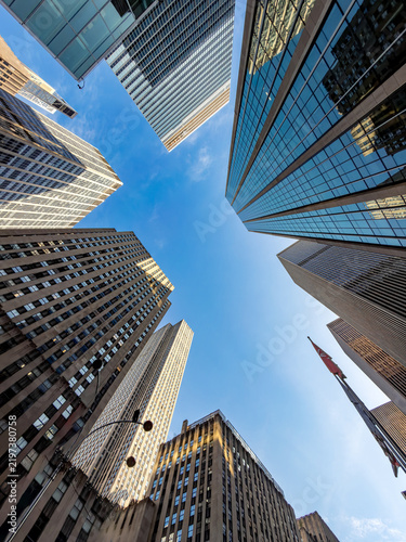 Upward perspective of glass office towers against blue sky. Worm eye view showing tall modern commercial skyscrapers surrounding a blue clear sky in Manhattan.