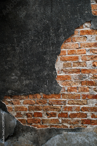 Old wall with damaged black plaster exposing red bricks underneath, representing building deterioration, aging, renovation, restoration, construction, maintenance, and urban decay.