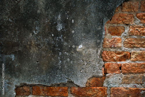 Old weathered wall with damaged dark plaster exposing red bricks underneath, representing building deterioration, aging, renovation, restoration, construction, maintenance, and urban decay.