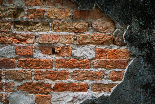Фотография Old weathered wall with damaged dark plaster exposing red bricks underneath, representing building deterioration, aging, renovation, restoration, construction, maintenance, and urban decay