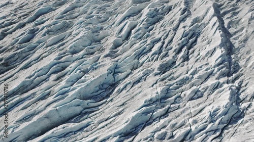 Aerial flight over a frozen glacier with deep ice cracks and crevasses. Natural cold landscape background. 