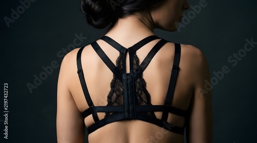 Woman wearing a stylish black lace strappy bralette against a dark background.