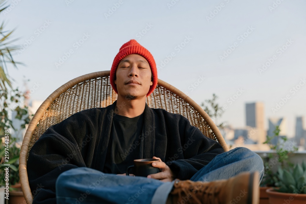 Fototapeta premium Rooftop portrait of relaxed man in red beanie holding a coffee mug for lifestyle banner and calm urban background design