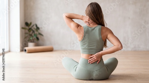 Young woman sitting on floor practicing yoga stretches for neck, spine, and lower back in bright studio
