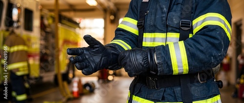 Firefighter in protective uniform putting on black leather gloves.