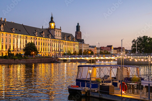 Cuadro en lienzo Waterside restaurant glows with lights along Oder embankment as Wroclaw skyline stretches behind