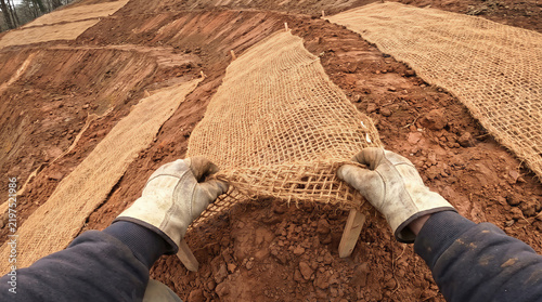 Installing biodegradable coconut coir geotextile netting for soil erosion control and land stabilization on a clay slope