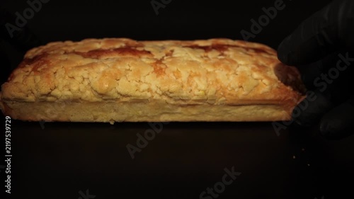 Close-up shot of a pastry chef in black gloves placing and adjusting a freshly baked hazelnut loaf cake on a dark surface. Perfect stock video for bakery ads, culinary tutorials, and dessert packaging