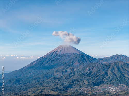 Canvastavla Volcanic Mount Semeru rises above forested slopes and rural settlements beneath a clear blue sky near Bromo Hill, Indonesia