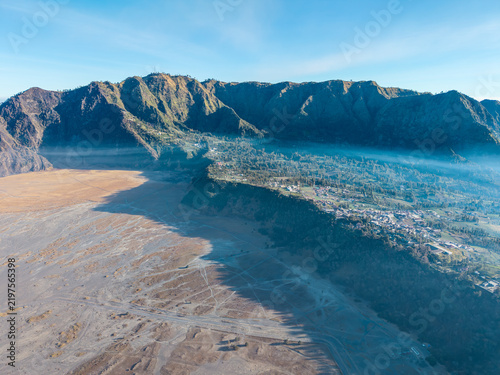 Obraz na płótnie Aerial panorama of Mount Bromo volcanic caldera, rugged ridges, sandy plain, mist, and rural settlements in Indonesia