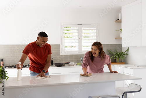 African American couple laughing and wiping countertop at home kitchen with spray bottle and cloths
