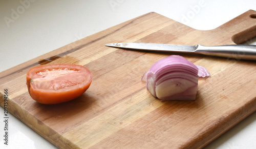 Fresh tomato and onion arranged with a kitchen knife on a rustic wooden cutting board, creating a simple food preparation scene for cooking and kitchen concepts.

